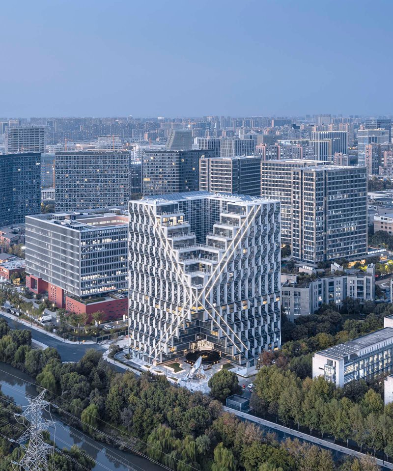 Twin tower forms joined at the base with latticed facades facing a dense urban skyline