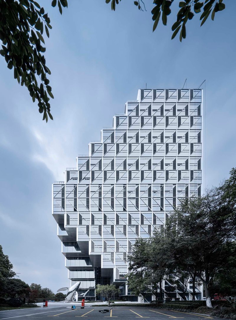 Street view of the ziggurat-shaped tower with its geometric white facade framed by tree branches