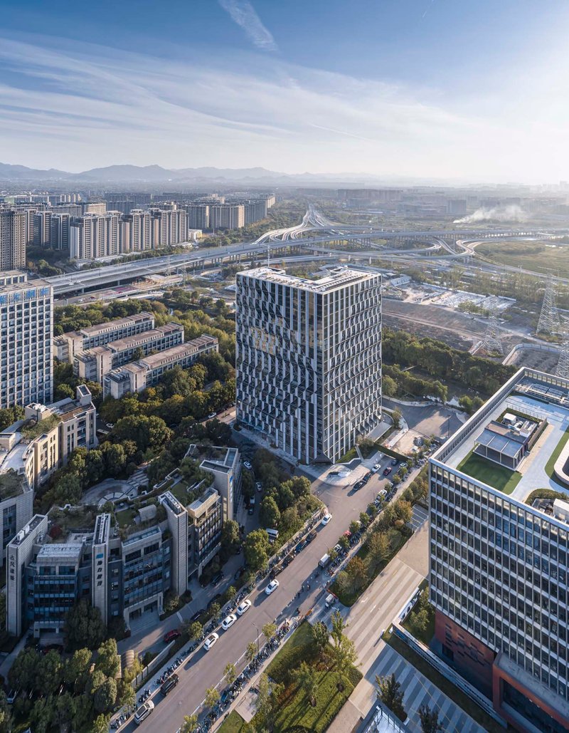 Drone view of the cylindrical tower with diamond-patterned cladding surrounded by highways and green space