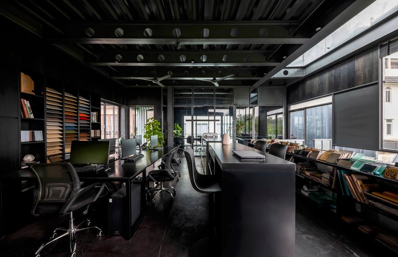 Open-plan office interior with exposed steel trusses, black furnishings and material sample shelving