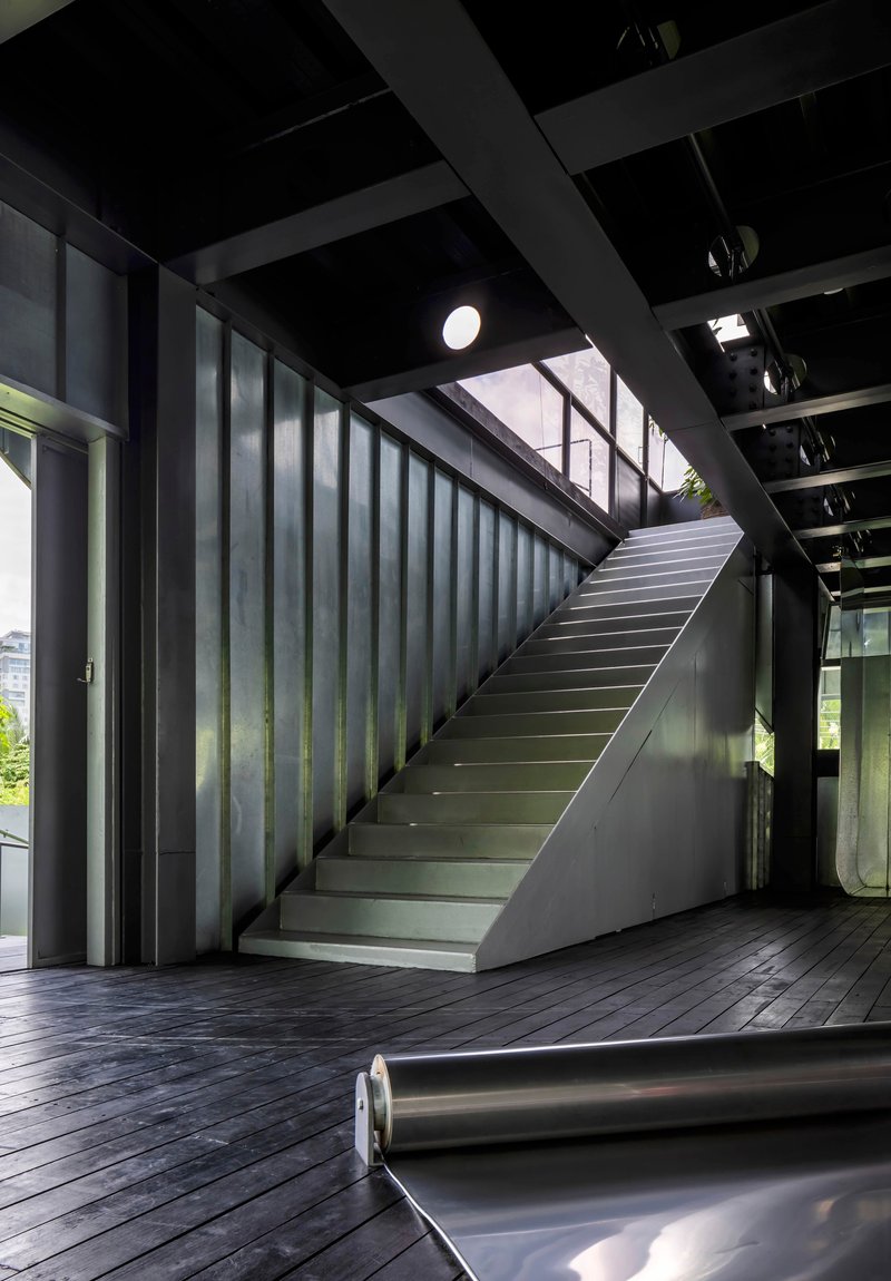 Interior staircase with blackened steel cladding and timber decking under an exposed beam ceiling