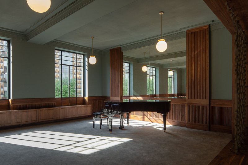 Interior room with grand piano, fluted wood paneling, globe pendant lights and afternoon sunlight streaming across floor
