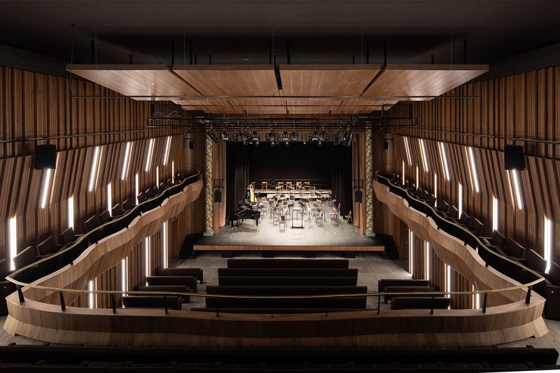 Concert hall interior with curved timber balconies, vertical lit slats and stage set for orchestra