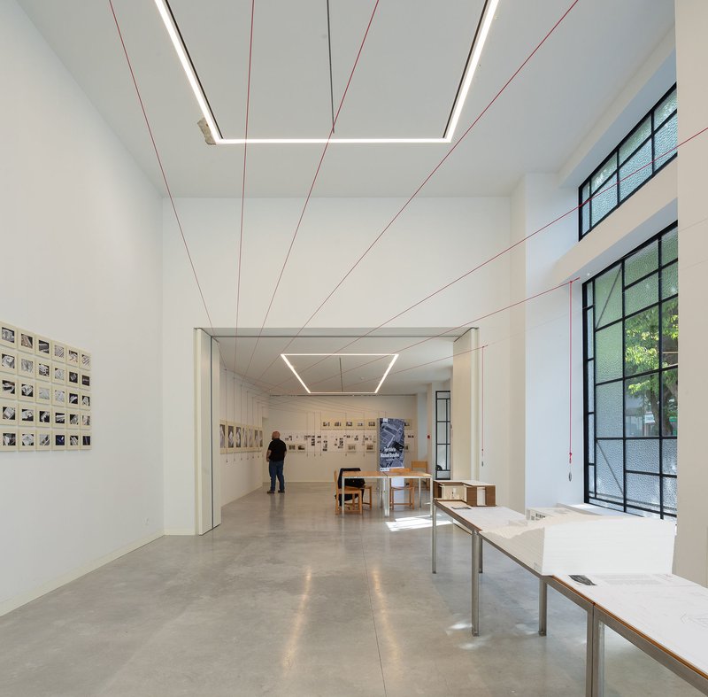 Gallery space with polished concrete floor, red tensioned cables and visitor viewing wall-mounted artworks