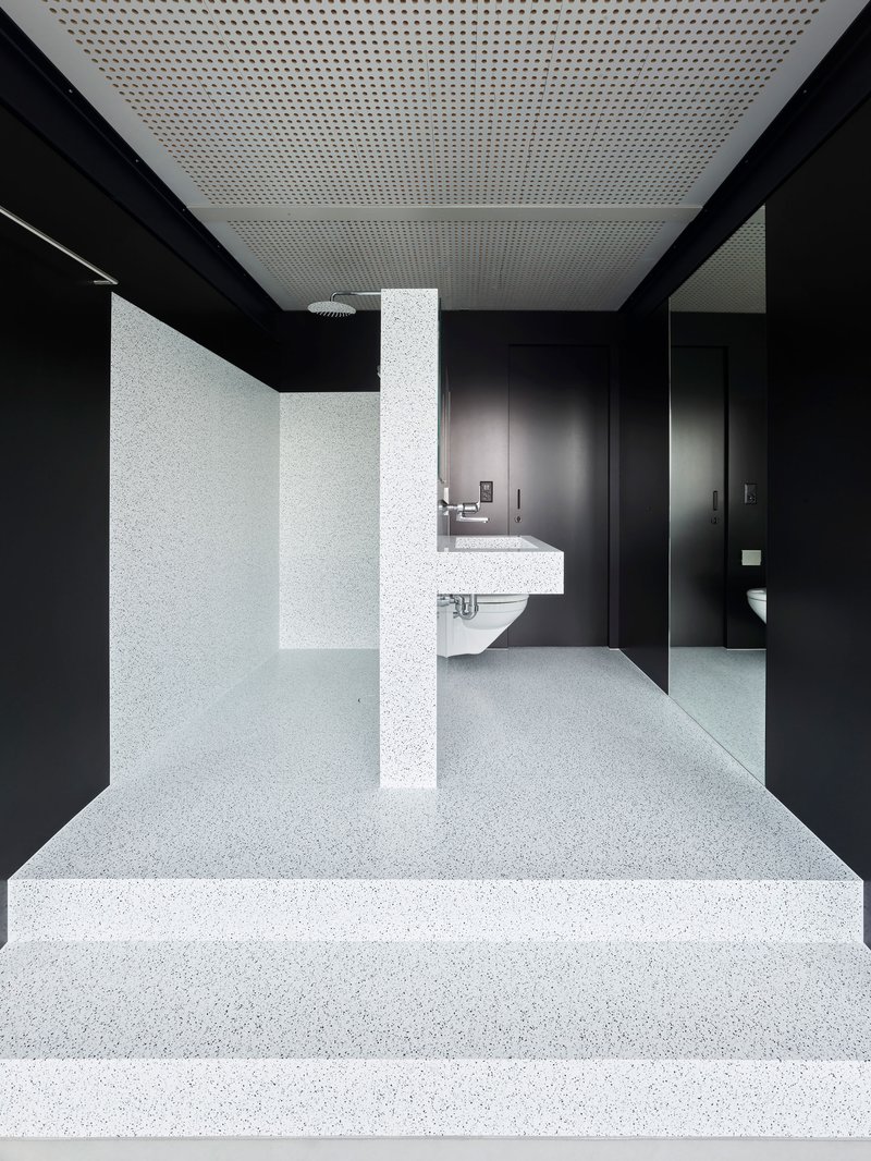 Terrazzo steps ascending toward a restroom with black walls and perforated white ceiling panels