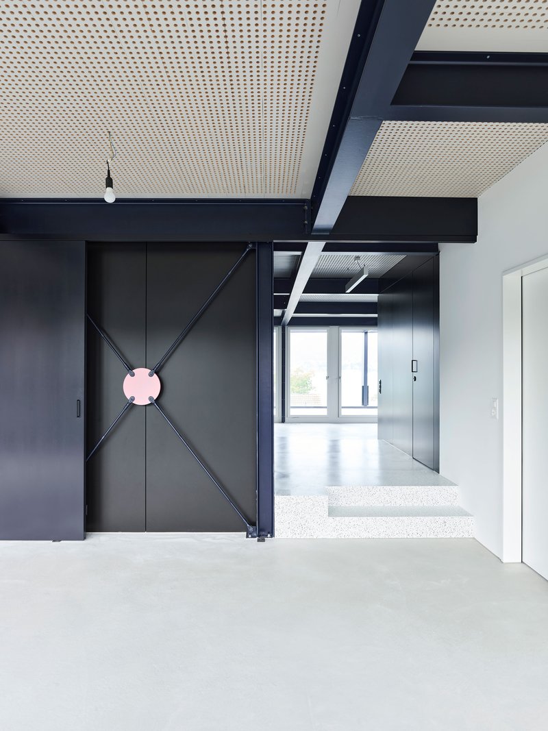 Black door with diagonal cross bracing and pink circular handle beneath perforated ceiling system