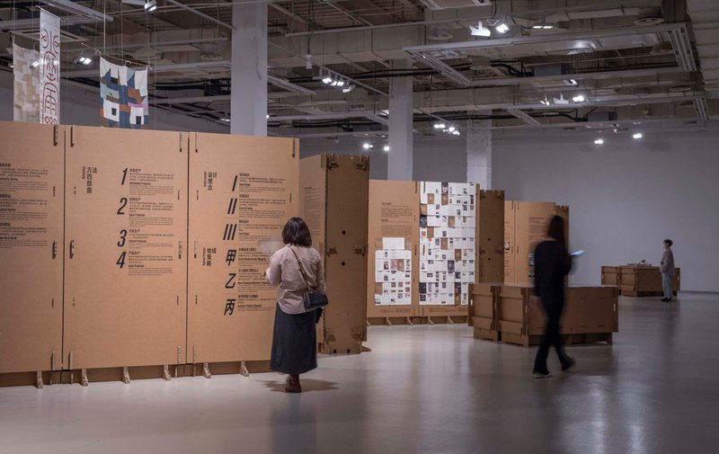 Visitor reading a cardboard information panel as other figures move through the gallery space