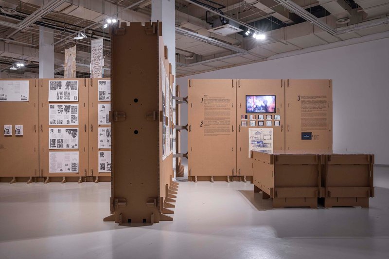 Cardboard wrapped structural column with slotted base and hinged display panels with embedded screen