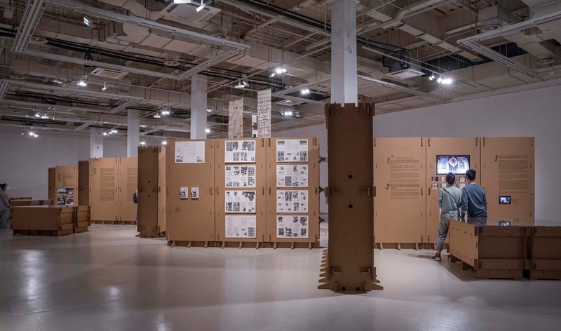 Installation of modular cardboard display systems with video monitors and photograph grids throughout the open hall