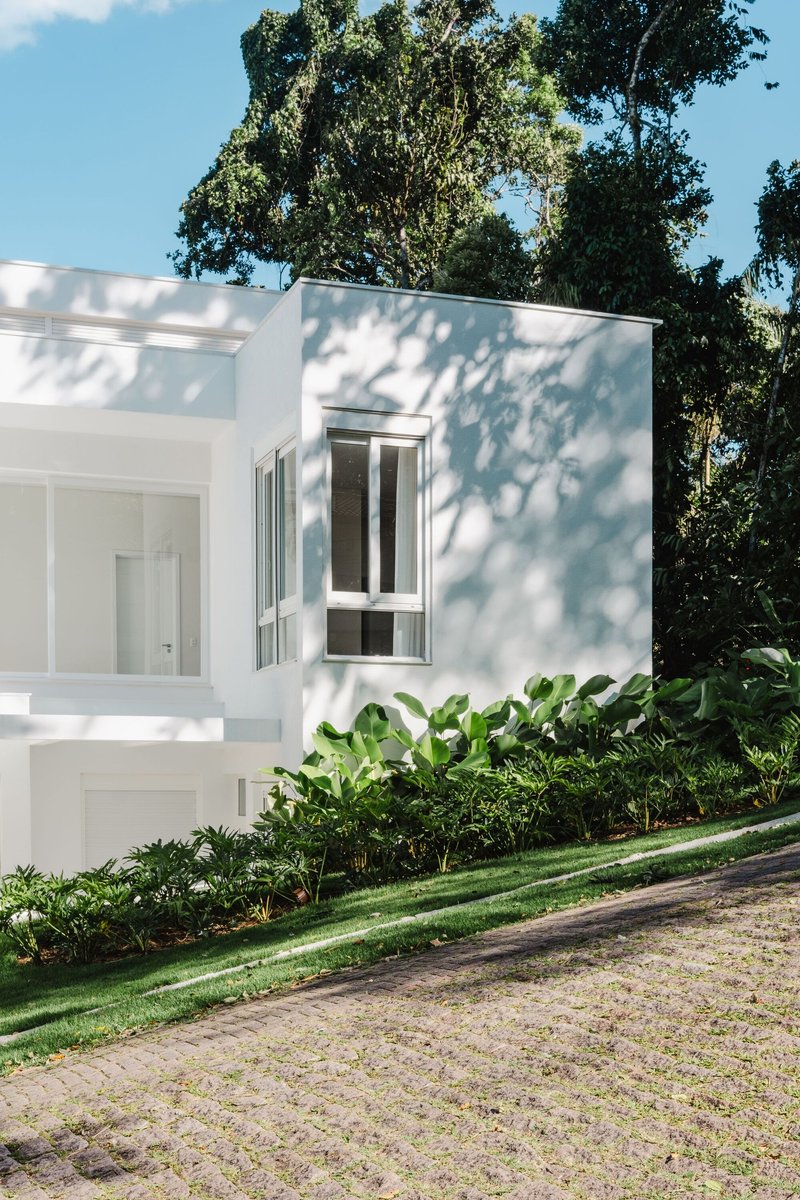 White rendered facade volumes framed by dense tropical foliage and dappled tree shadows