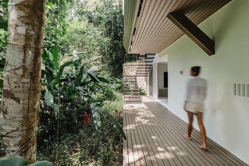 Timber-decked walkway with slatted ceiling overhang leading past planted garden beds with a person in motion