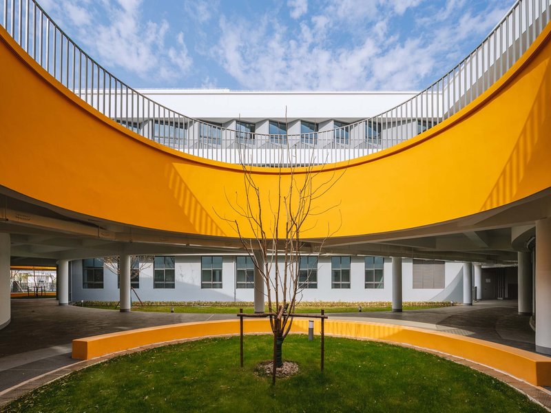 Orange curved balcony framing a courtyard with a young tree and lawn under blue sky