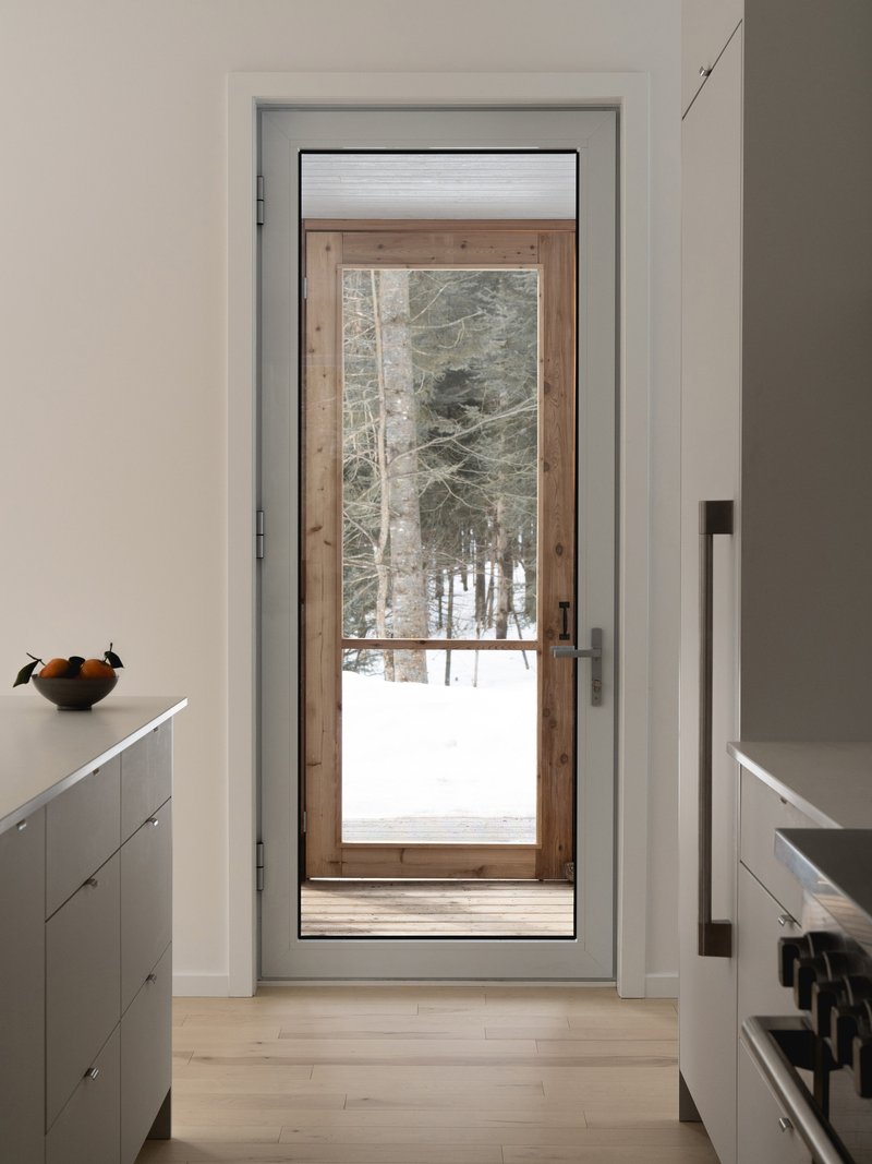 View through a white-framed doorway to a timber-and-glass exterior door with snowy woods beyond