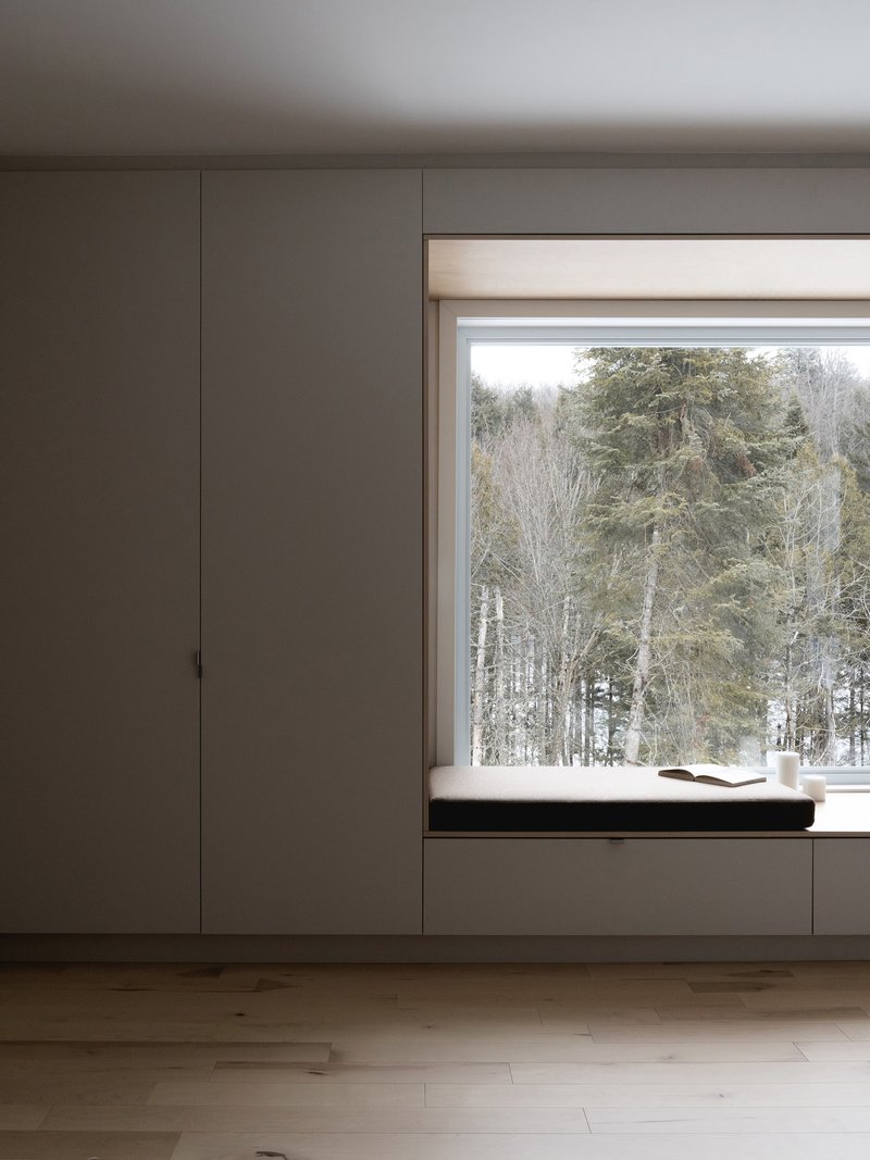 Built-in window seat with timber frame and grey cabinetry facing a winter birch forest