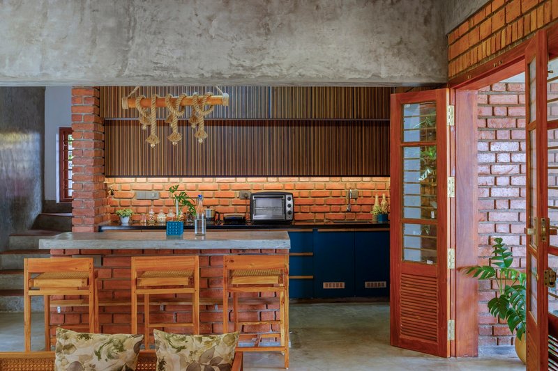 Kitchen with exposed brick island, timber slatted upper cabinets and brass pendant lights beneath a raw concrete ceiling