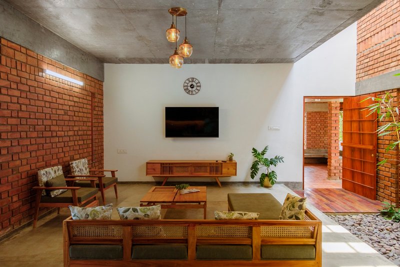 Living room with exposed brick walls, wooden furniture and three brass globe pendants below a concrete vault ceiling