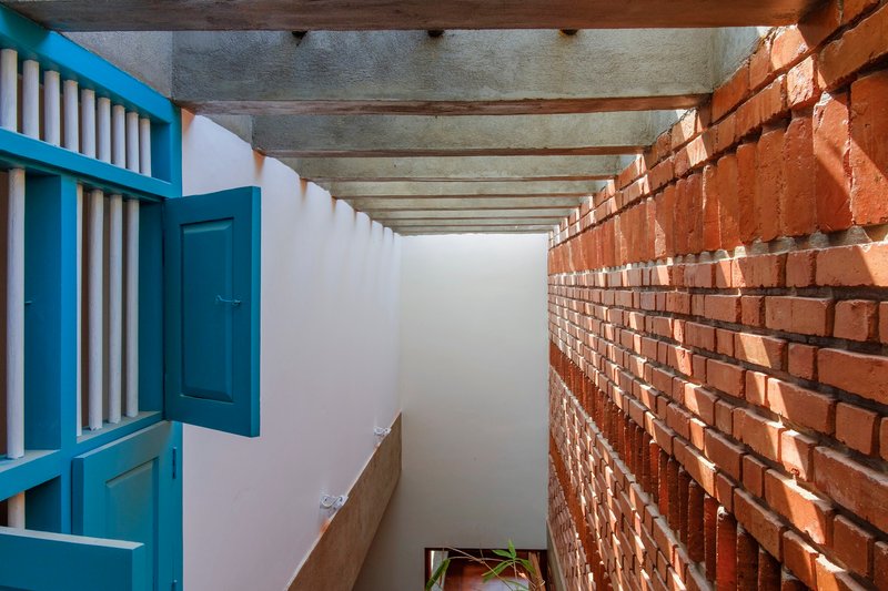 Corridor with exposed brick wall on one side and blue painted timber screen on the other under concrete beams