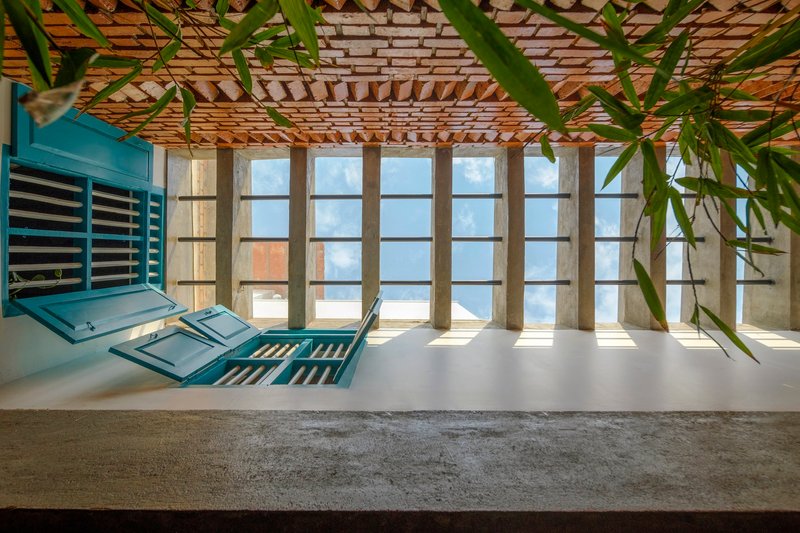 Terrace with blue louvered shutters, bamboo overhead trellis and concrete framed glazing under bright afternoon light