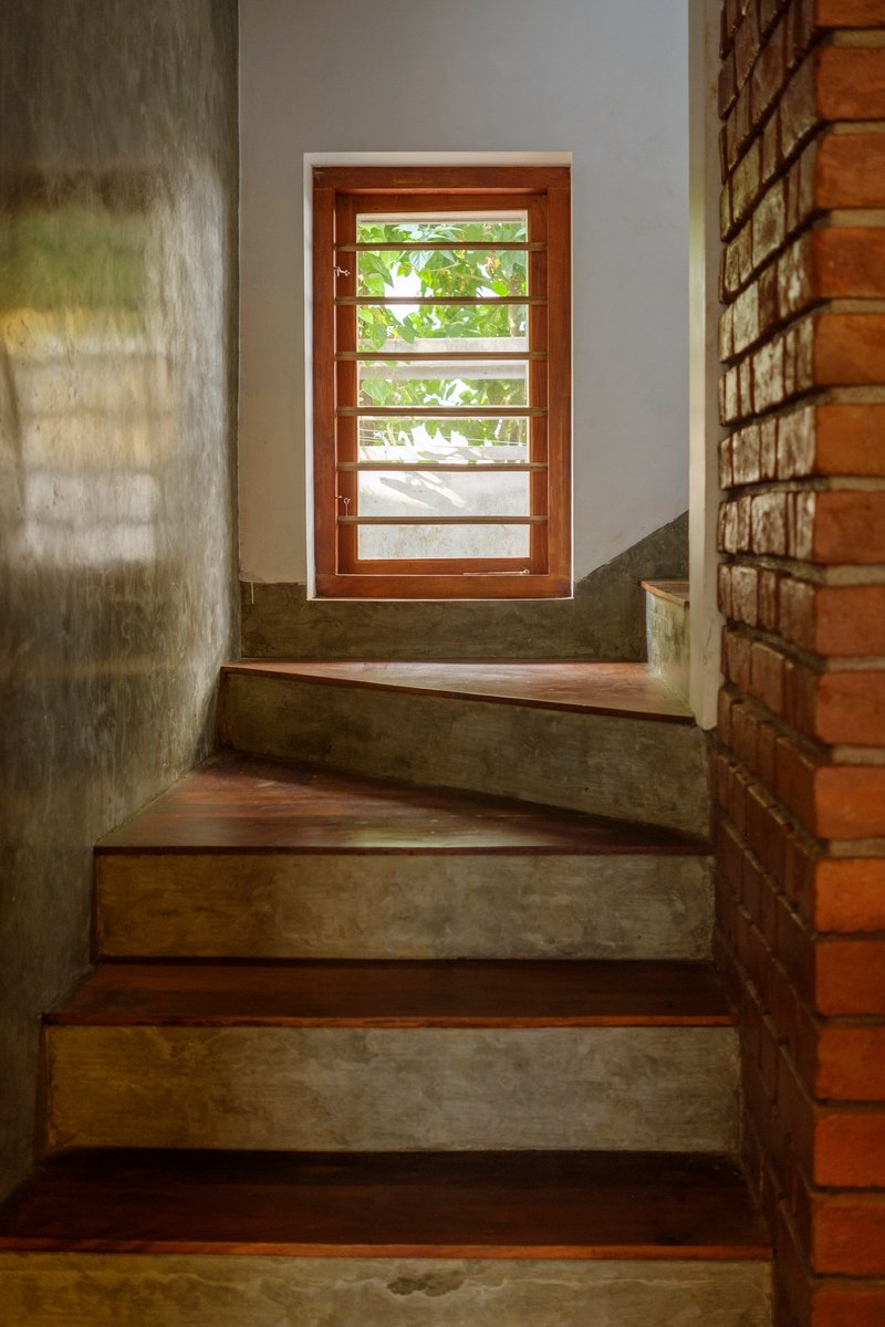 Interior staircase with alternating wood and concrete treads leading to a horizontal louver door with green foliage visible beyond