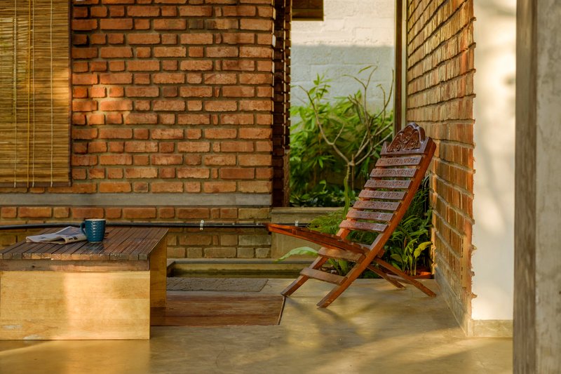 Covered terrace with exposed brick walls, folding wooden chair, and low platform bed in dappled afternoon light