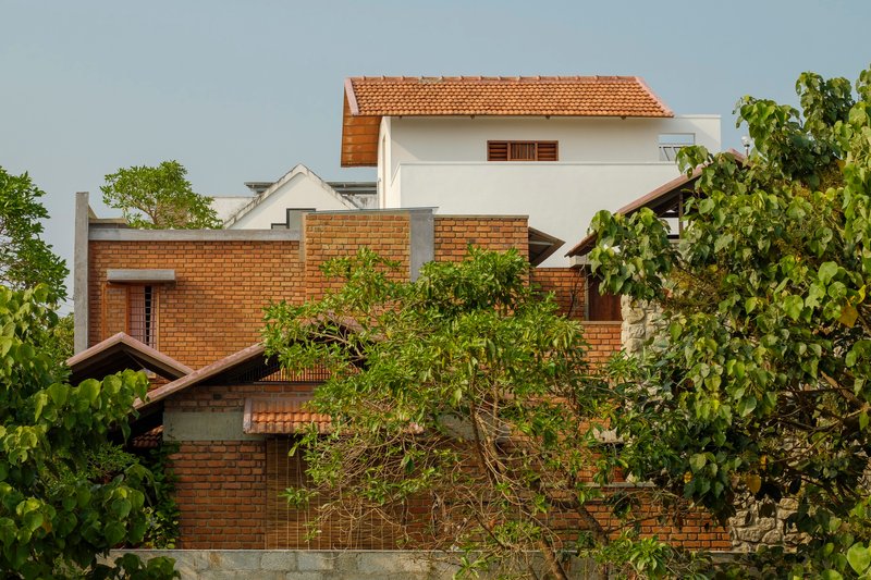 Layered brick volumes with clay tile roofs rising above surrounding trees and foliage