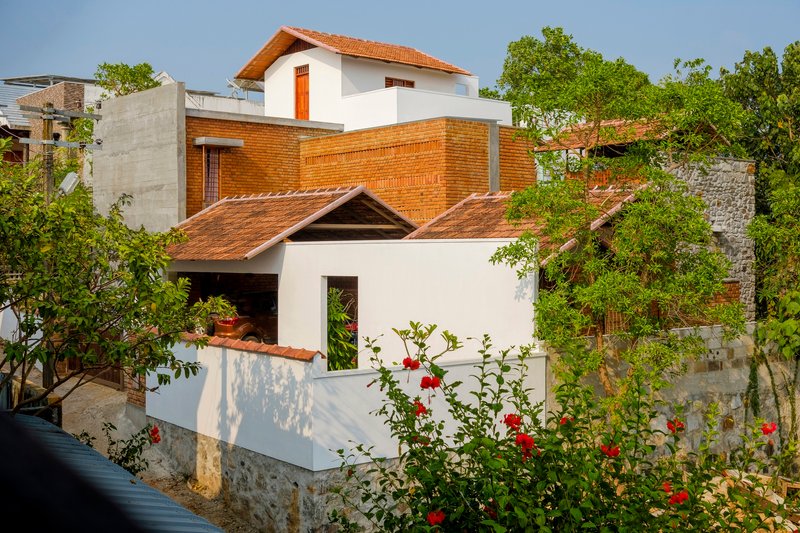 Street view of the stacked volumes and gabled roofs surrounded by flowering roses