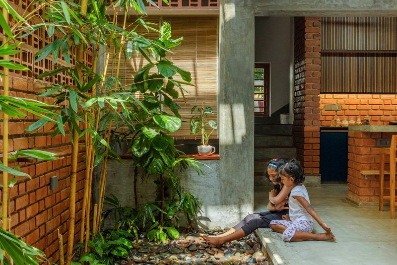 Interior courtyard with concrete columns, exposed brick walls and two children seated by planted greenery