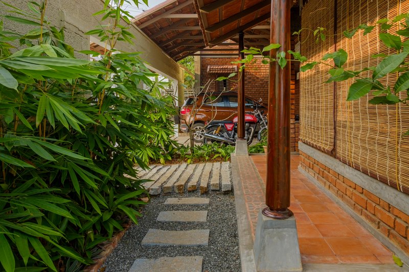 Covered walkway with timber columns and stepping stone path beside planted beds and bamboo screens