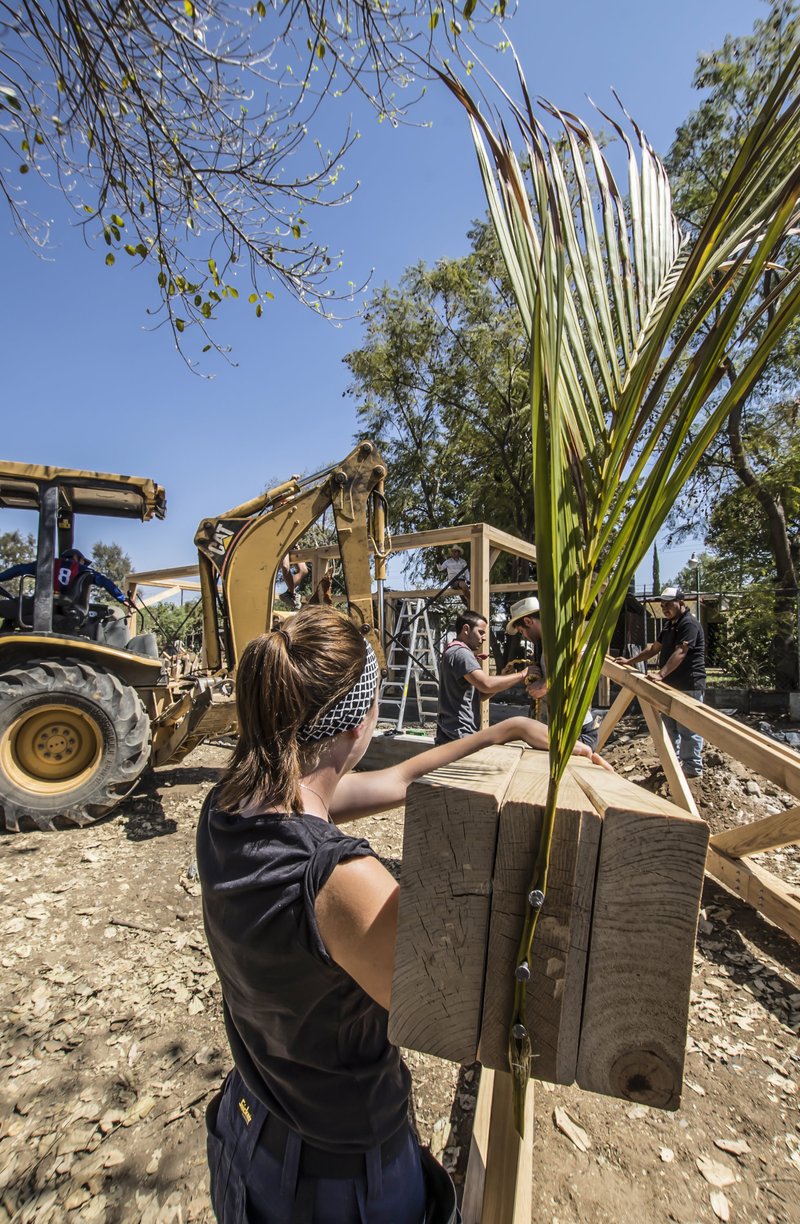 Construction site with workers assembling timber framework and palm fronds under a clear blue sky