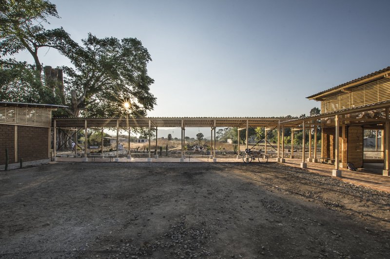 Covered courtyard space with corrugated metal roof and timber columns viewed at dusk with surrounding landscape