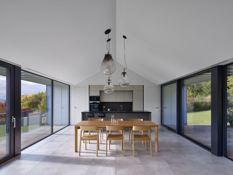 Open dining area with timber table and glass doors to exterior terraces beneath a vaulted white ceiling