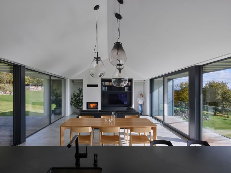 Interior view through dining and living spaces with glass pendant lights and a person visible on the exterior deck