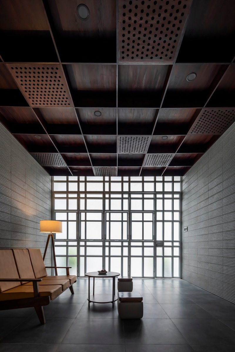 Seating area beneath perforated metal ceiling panels with gridded glass wall beyond