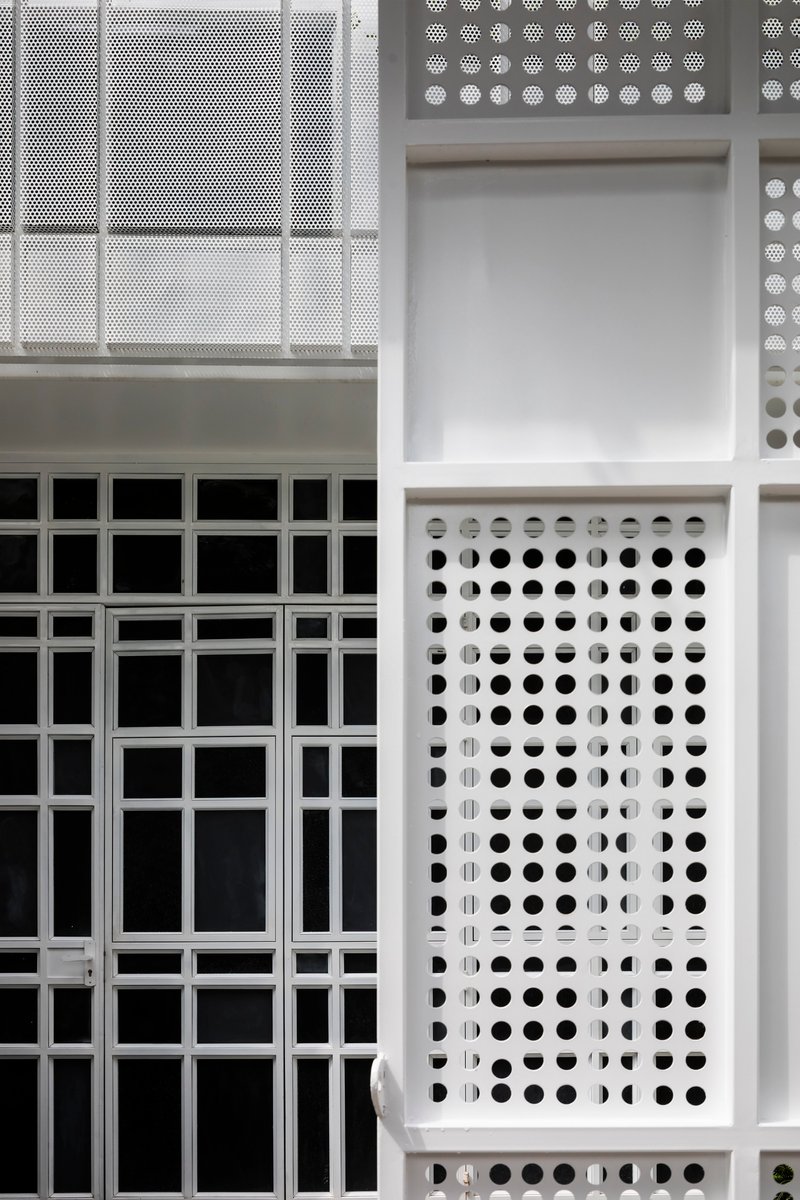 Close-up of white metal facade panels showing perforated and solid modules in a grid
