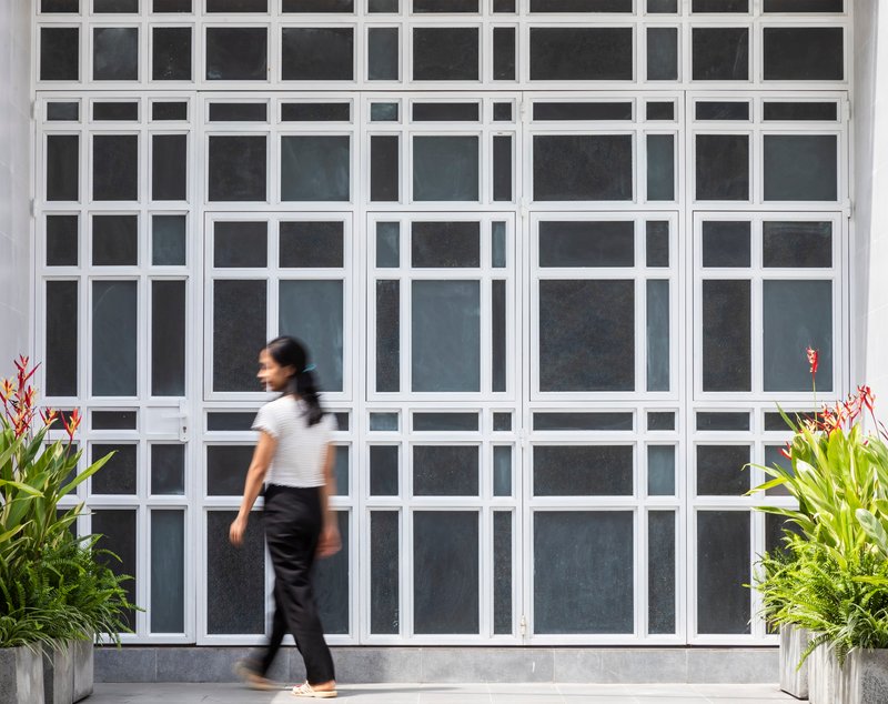 White gridded metal screen facade with a person walking past potted plants