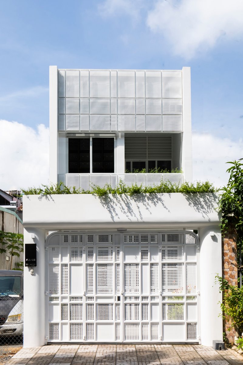 Street-facing facade with white perforated metal gates below a grid of frosted glass panels and planted rooftop
