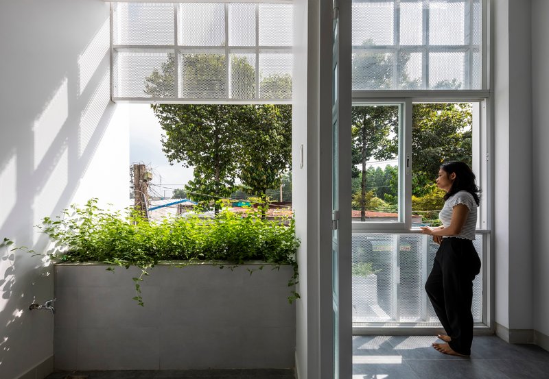 White interior balcony with planted concrete planter and a woman looking out through full-height glazed doors