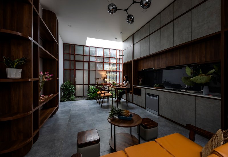 Open kitchen and dining space with dark timber cabinetry, concrete panels, and translucent gridded screen wall