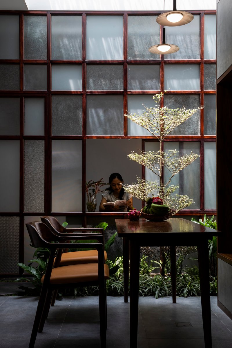 Woman reading at the dining table with a small tree and translucent screen wall behind her