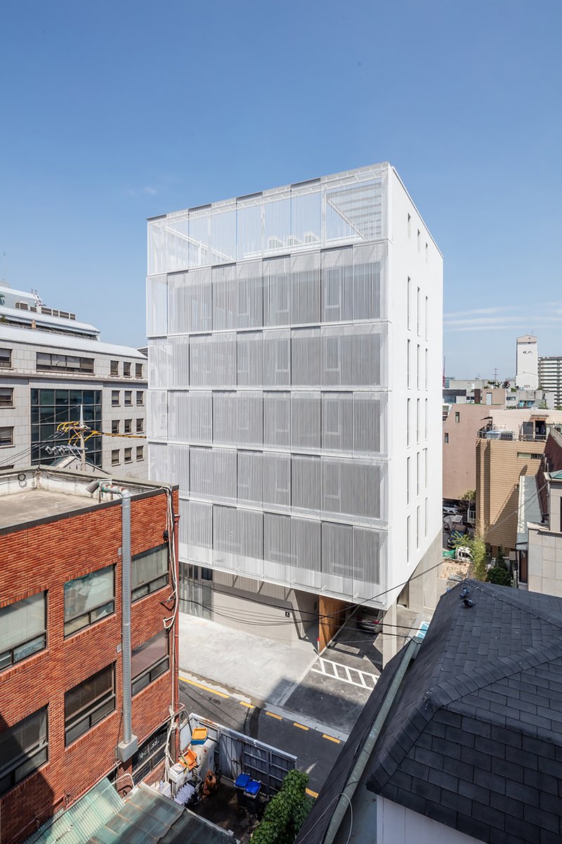 White translucent panel facade rising above neighboring brick buildings and tiled rooftops under clear sky