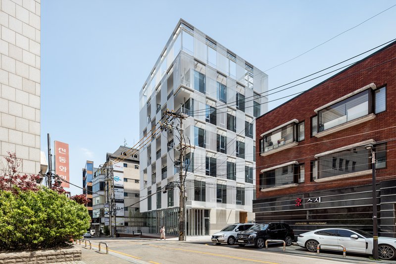 Street view of the white ribbed facade flanked by red brick buildings and utility poles