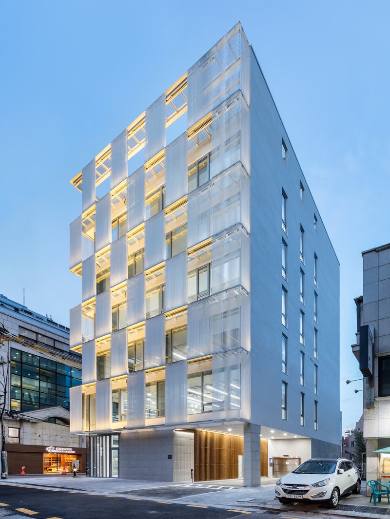Street view of the white louvered tower facade illuminated at dusk with parked cars in front
