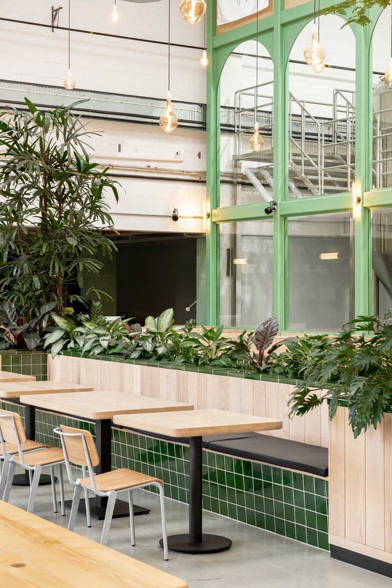 Interior seating area with light wood booths, green tile base and painted green steel partition framing