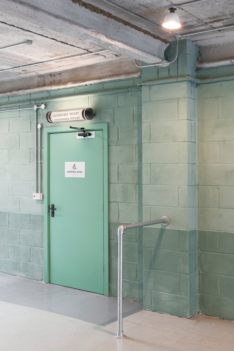 Mint green steel door with exposed conduit and concrete block walls under an industrial ceiling