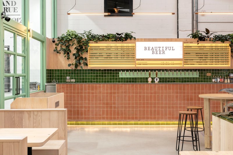 Frontal view of the tiled bar with timber-framed backlit signage and hanging plants cascading from planter boxes