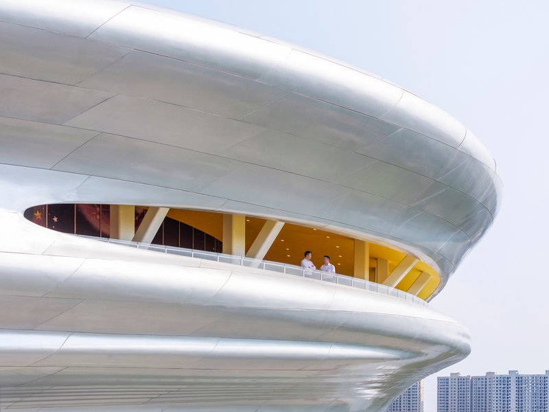 Close-up of two curved balcony levels with two visitors standing at the railing under an overcast sky