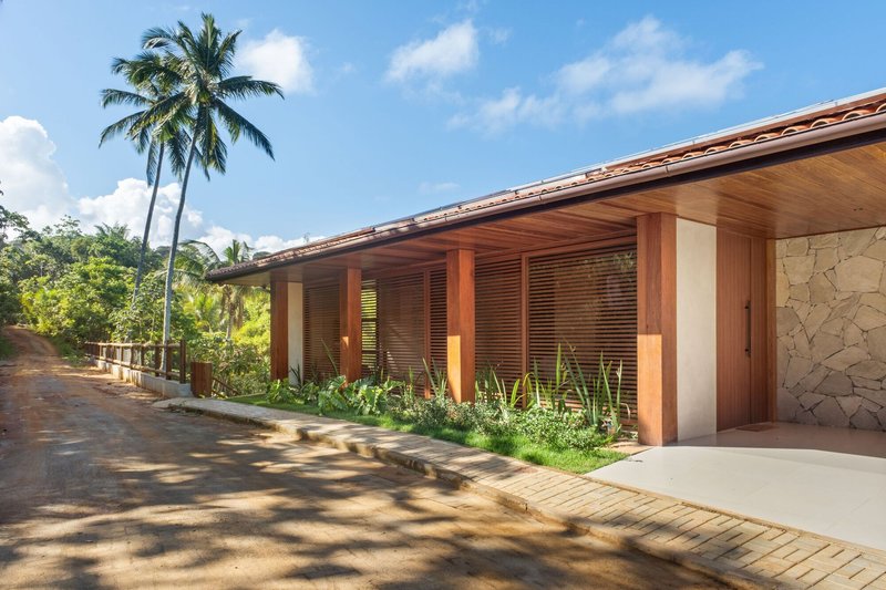Long facade with timber columns and louvered screens along a planted bed with palm tree overhead