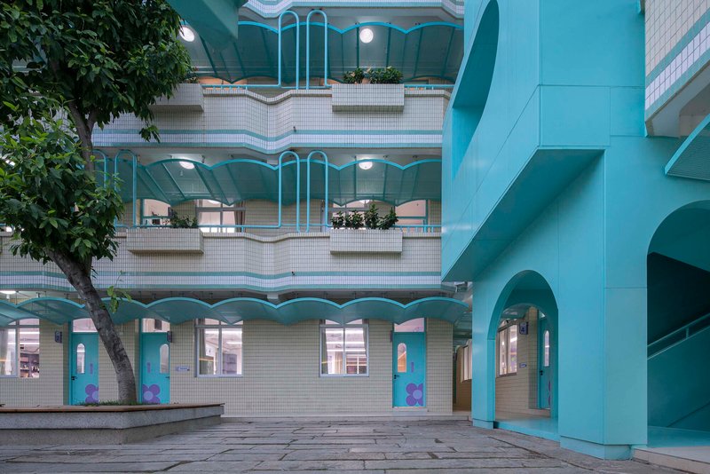 View across a paved plaza showing tiered balconies with wavy white railings and potted trees