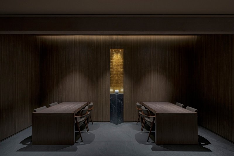 Private dining room with mirrored timber tables flanking a vertical black marble niche with gold leaf
