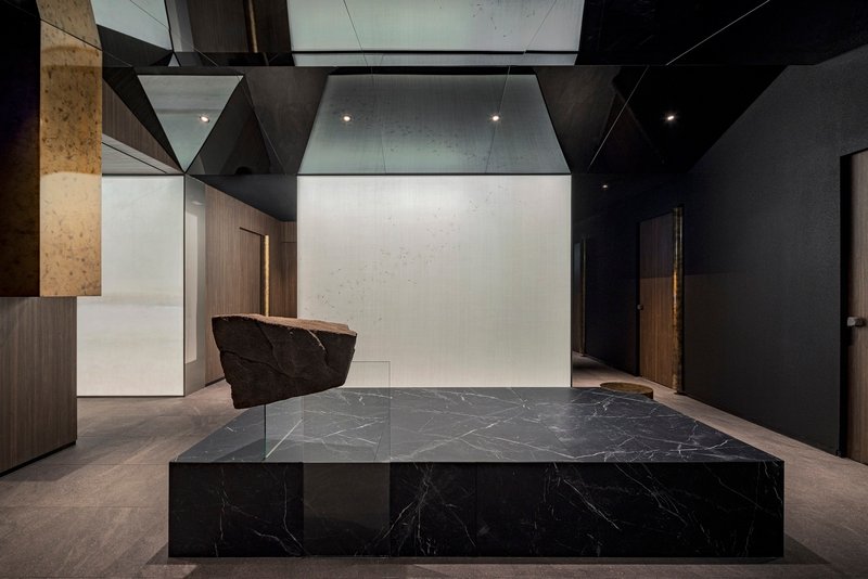 Black marble reception counter with a tree trunk fragment suspended from the faceted ceiling above